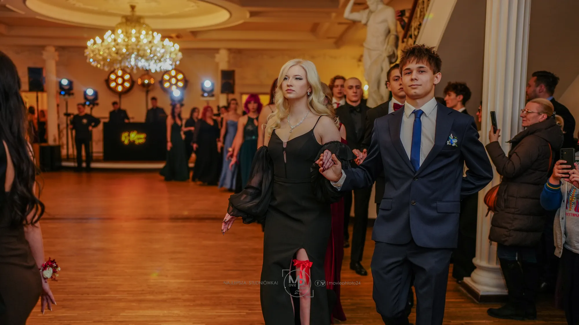 Para przechodzi przez salę w świetle żyrandoli